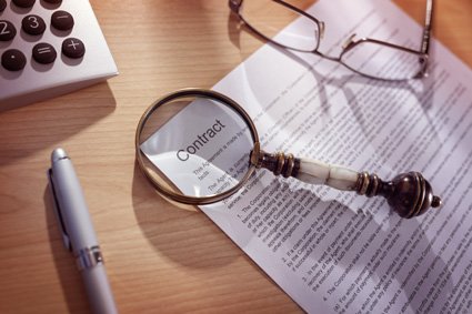 A magnifying glass is laid on top of a legal contract representing how important it is to read and understand the terms and conditions of a merchant processing contract when considering a payment processing solution law firms will best benefit from.